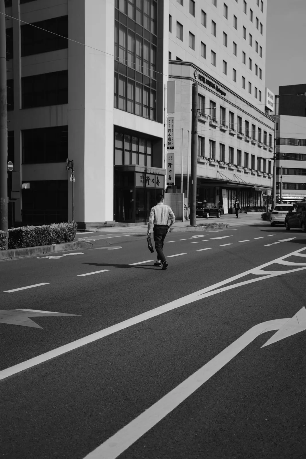 Black and white photo of a person crossing a wide city street between office buildings