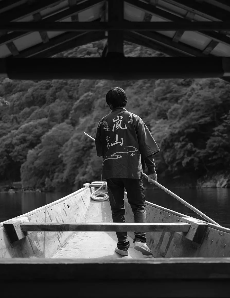 Person standing at the back of a wooden boat on a calm river with forested hills behind