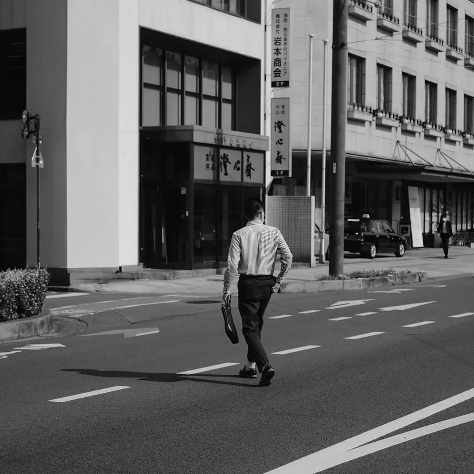 Man carrying a briefcase across a wide city street between office buildings