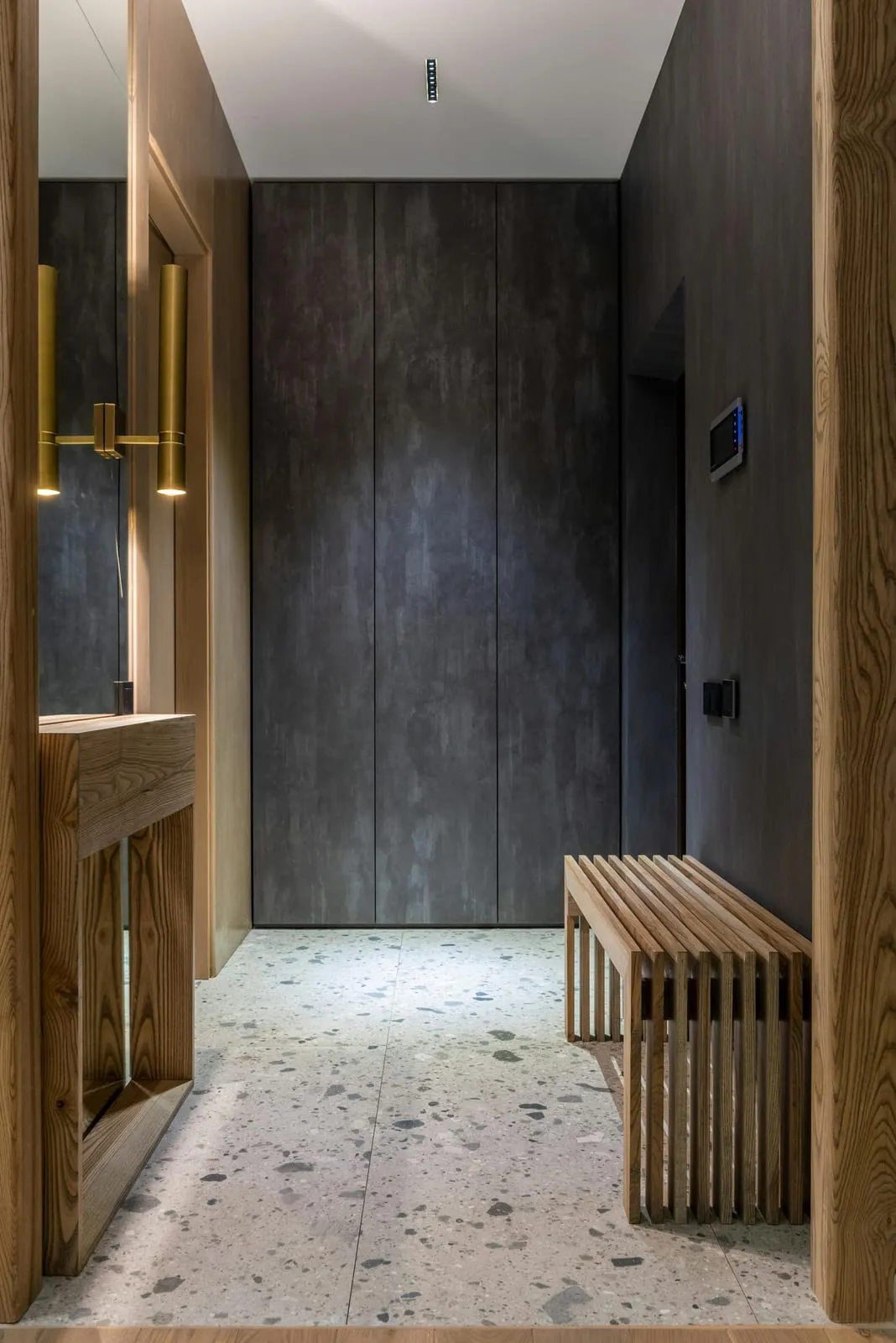 Entryway with a dark stone wall, brass wall lights and a wooden bench