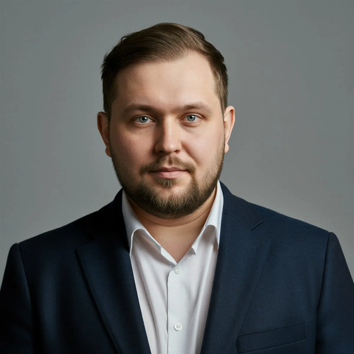 Bearded man in a dark suit jacket and white shirt against a grey background